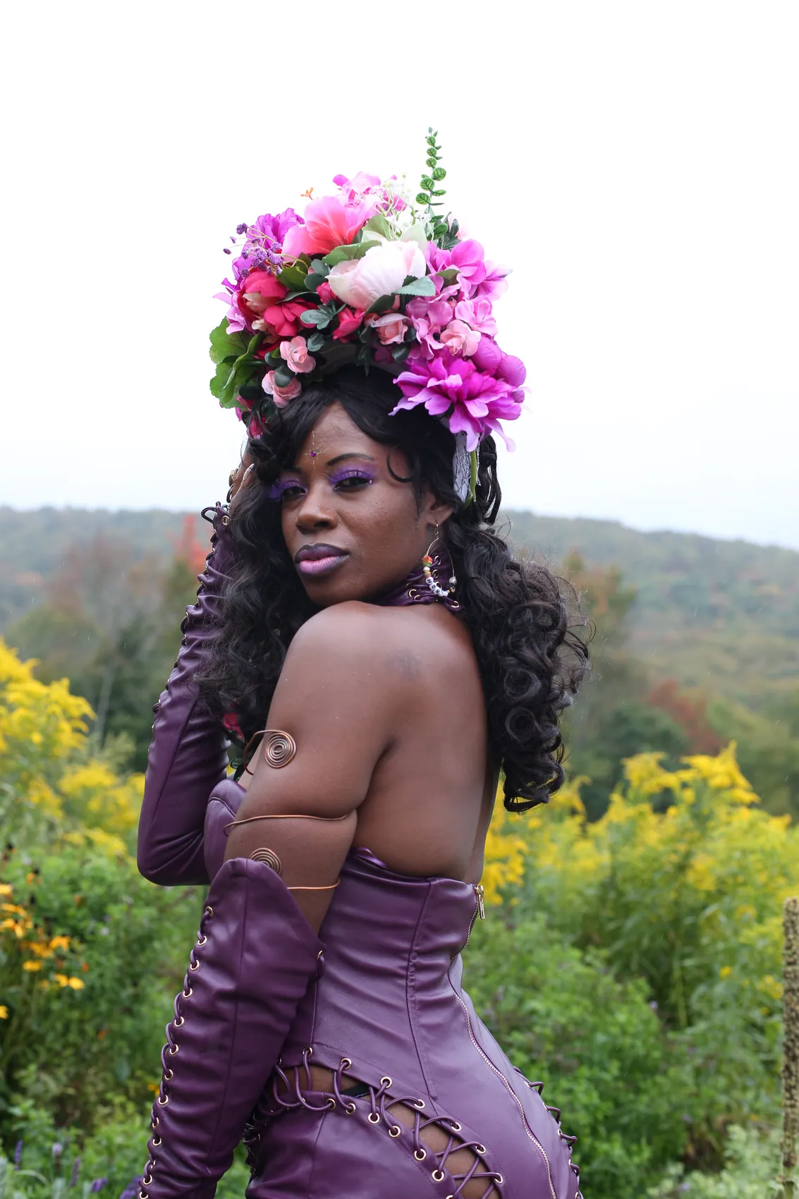 A woman in a purple corset gown looking over her shoulder, wearing a crown of pink and magenta flowers