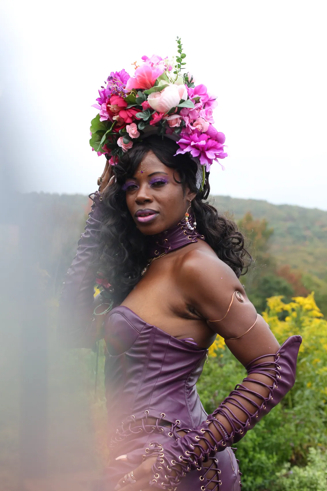 A woman in a purple corset gown in a magenta flower crown against the hills