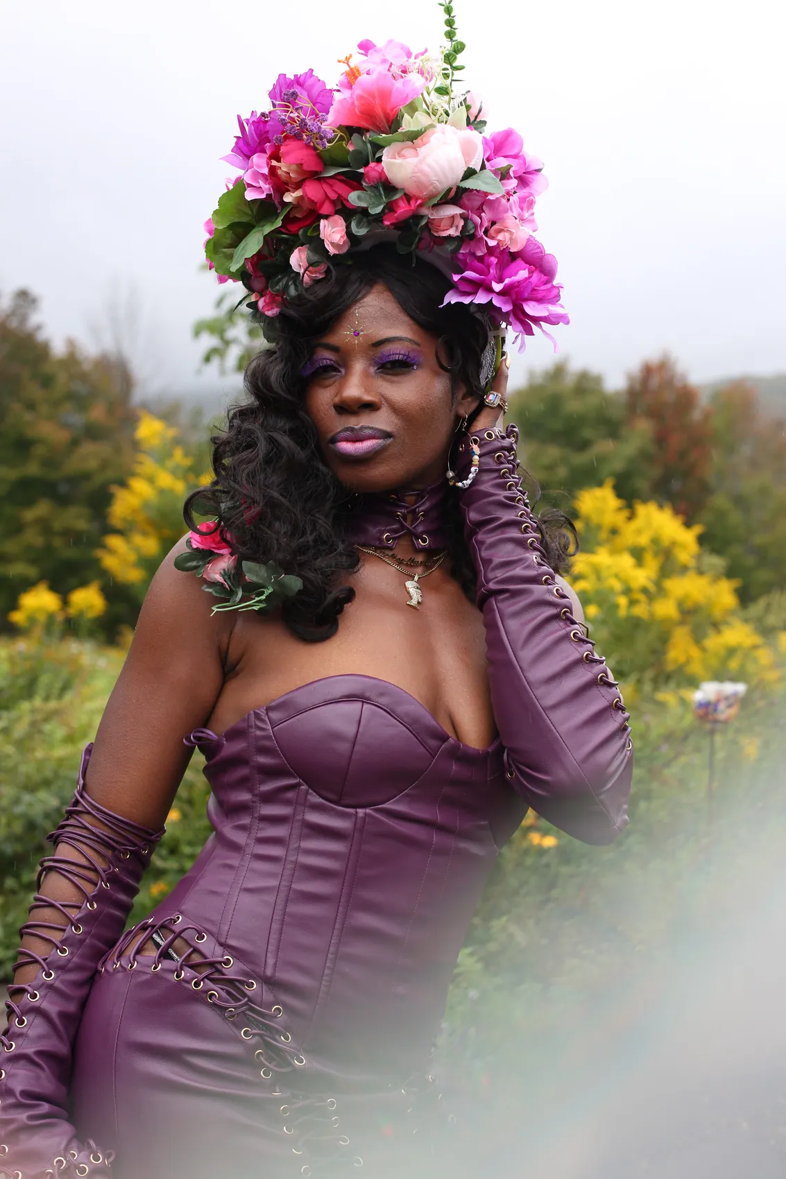 A woman in a purple leather corset dress wearing a crown of pink and magenta flowers