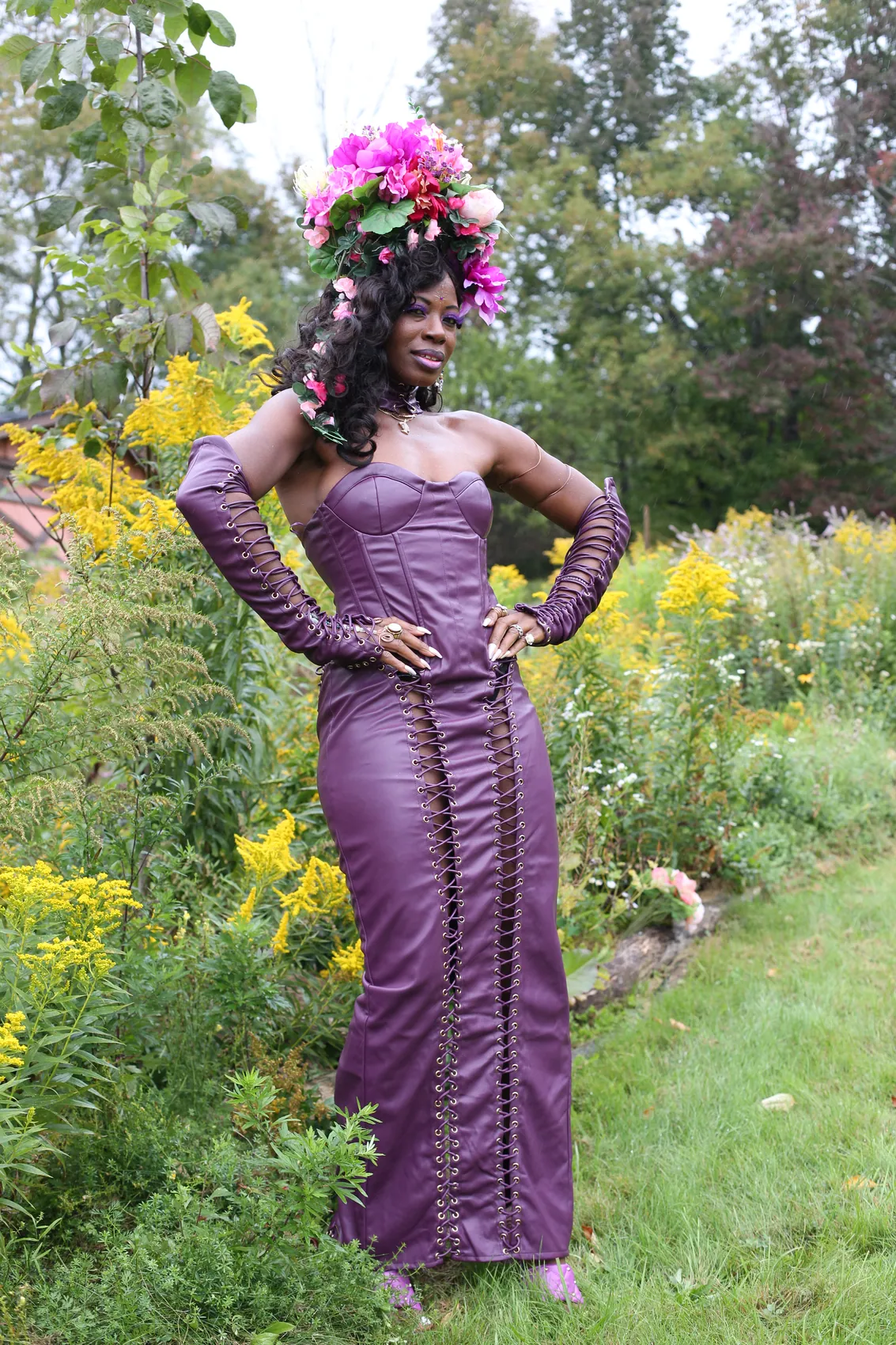 A woman posing with hands on hips in a purple gown and pink crown