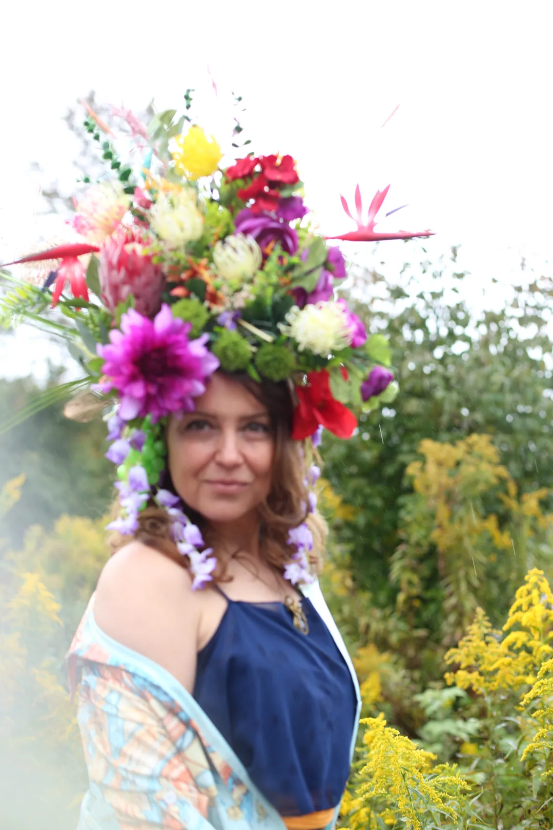 A woman in a navy dress and pastel kimono wearing a crown with a purple dahlia and wisteria