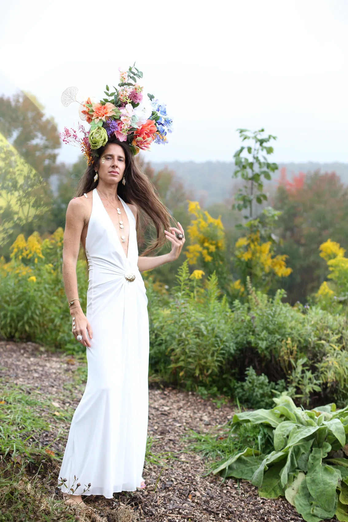 A woman in a long white gown and a tall peach crown, one hand in her hair