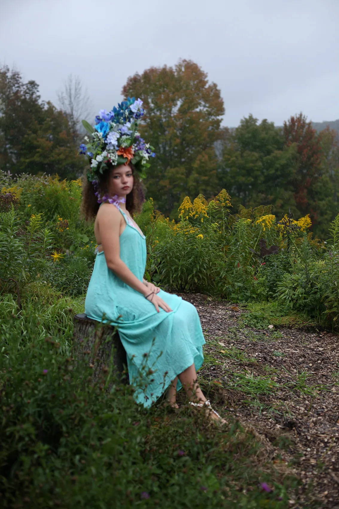 A young woman in a turquoise dress seated in a crown of blue delphinium