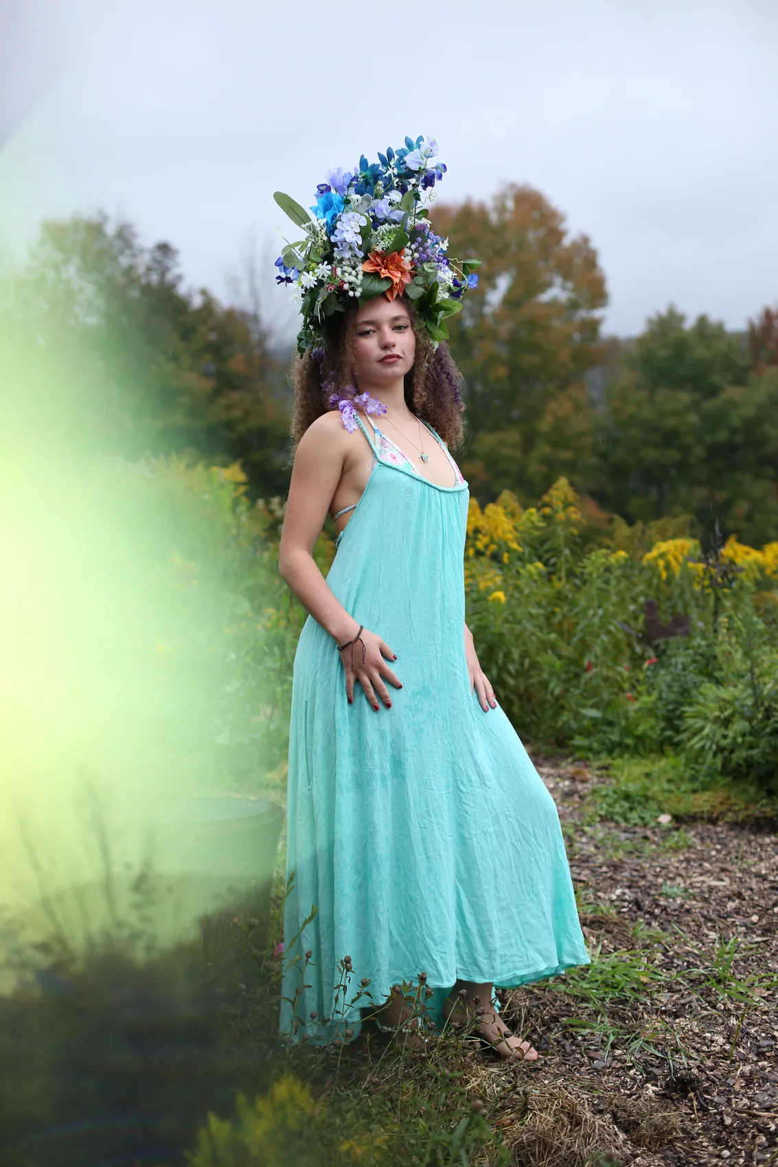 A young woman in a turquoise dress standing in a meadow in a crown of blue flowers