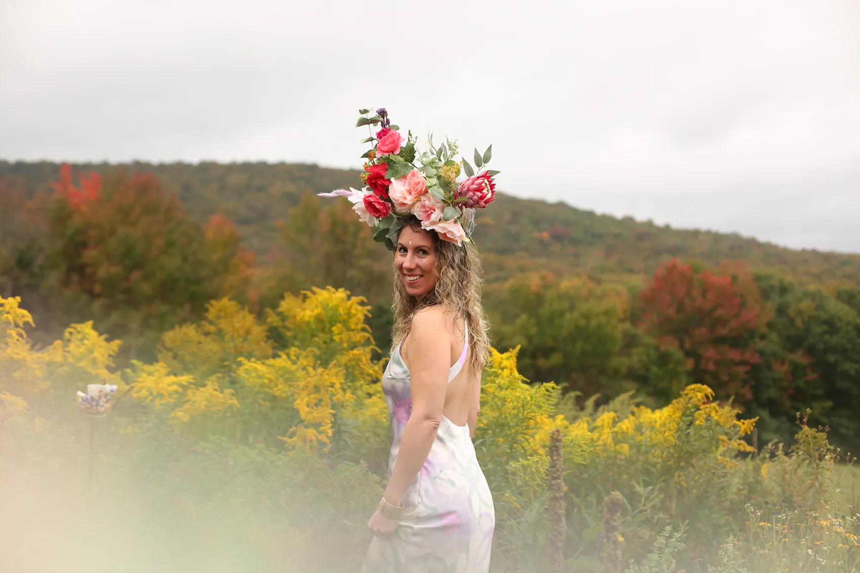 A woman smiling over her shoulder in a crown of pink roses among goldenrod