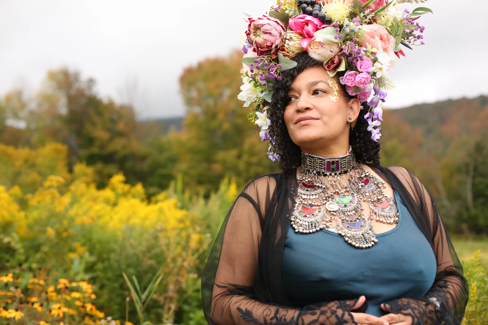 A woman in teal and black lace looking over the meadow in a crown of protea and lilac