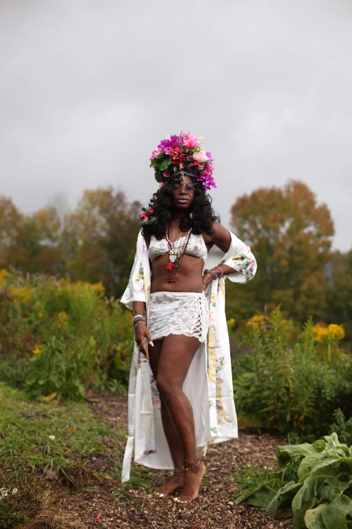 A woman in white lace and a silk robe wearing a magenta crown, full-length