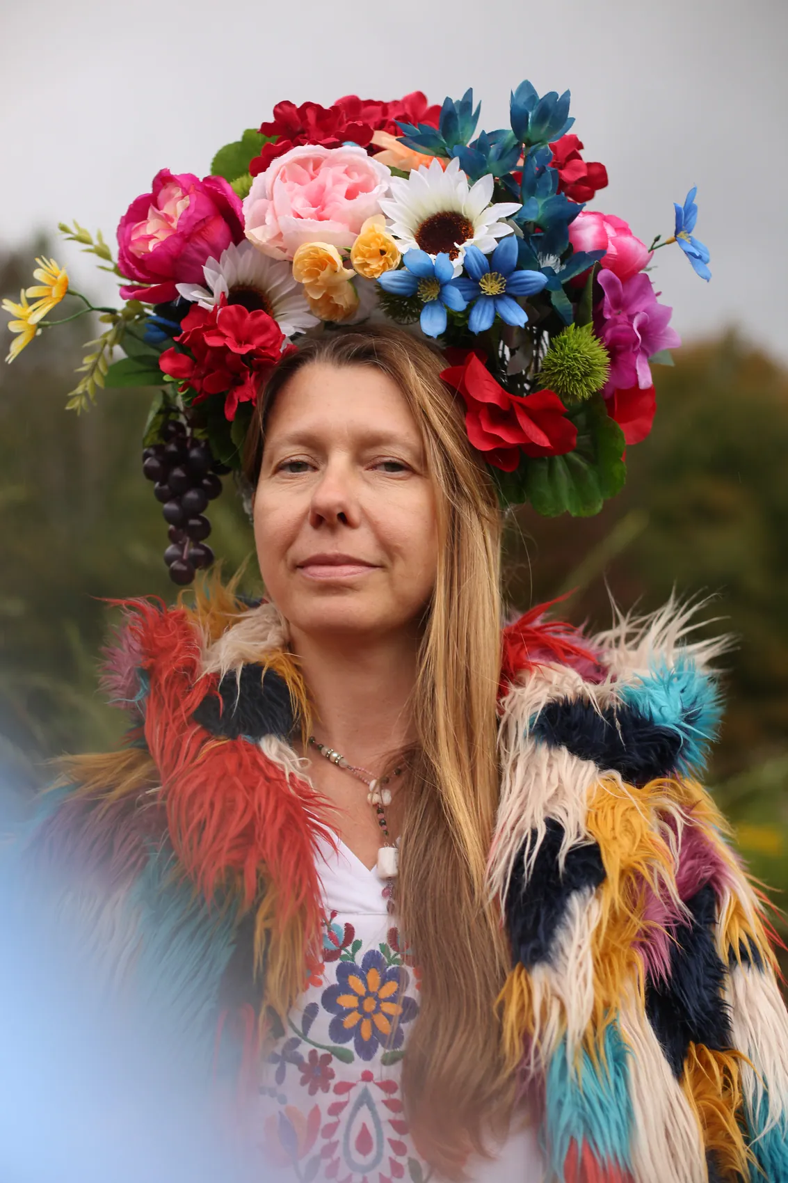 A woman in a rainbow fur coat wearing a crown of peonies, daisies and blue lilies