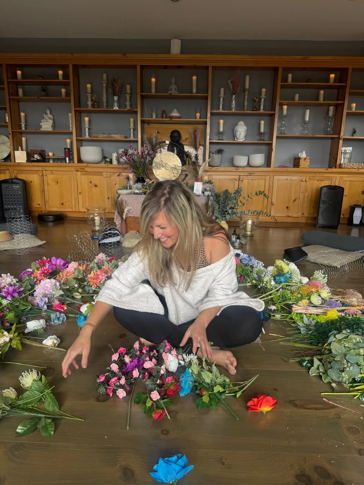 Daniela sitting on the floor among piles of silk flowers, laughing as she sorts blooms for a crown